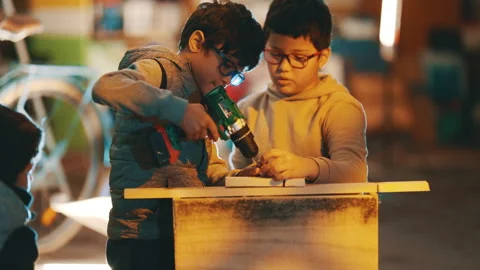 Curious boys learning woodworking with a power drill Stock Footage 329559700