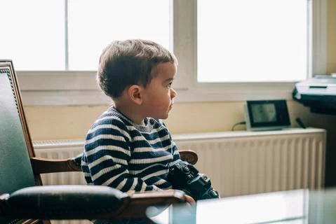 Curious child explores camera sitting on a chair Stock Photos