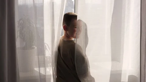 Curious child looks out the window, eyes wide with wonder. Child gazes through Stock Footage 275813639