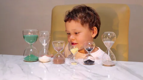 Curious child playing with many different hourglasses on table Stock Footage 300370507