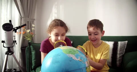 Curious children exploring globe with magnifying glass, sitting in warm sunlight Stock Footage 313079513
