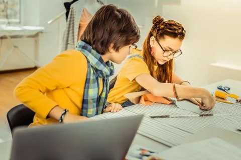 Curious dark-haired brother watching his sister drafting patterns Stock Photos