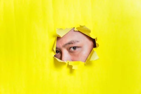 A curious eye peeks through a torn yellow paper backdrop. Stock Photos