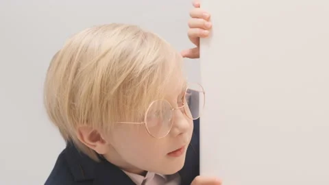 Curious fair-haired boy with big glasses peeking around the corner Video stock 172487326