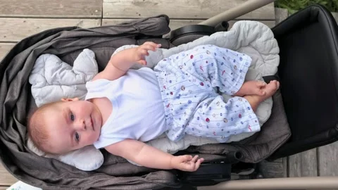Curious infant looks around while lying in a stroller outdoors, baby Video stock 340189828