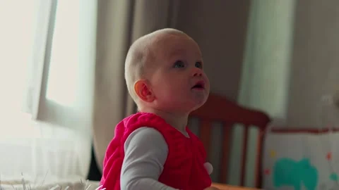 Curious infant looks around while seated at a table in a softly lit nursery at Stock Footage 347686929