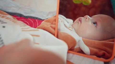 Curious infant lying next to mirror, Playing baby reflection in the mirror Stock Footage 246560984