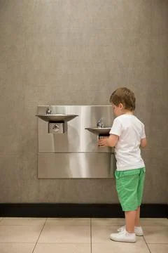 Curious kid boy drinking water from drinking fountain. Stainless Steel drinki Stock Photos
