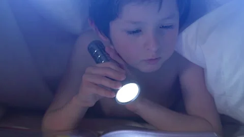 Curious little boy enjoying reading interesting book lying under blanket in bed Stock Footage 130466160