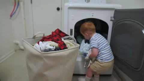 Curious little boy loading laundry into washing machine with colorful clothes Stock Footage 320147275