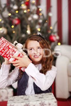 Curious little girl shaking her christmas gift Stock Photos