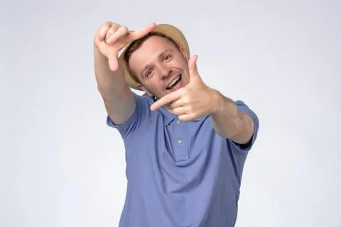 Curious man in summer hat gesturing picture frame with hands, looking through Stock Photos