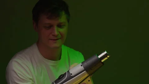 Curious man in white t shirt inspecting heat gun, turning it on and looking at Stock Footage 342809889