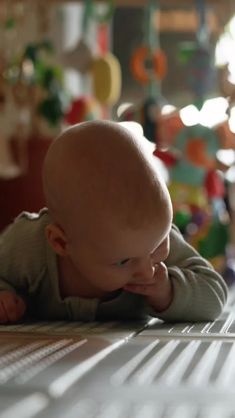 Curious newborn lying on play mat during tummy time, sunlight casting shadows Stock Footage 344256308