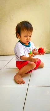 Curious one year old holding a vibrant healthy snack on the steps 스톡 사진