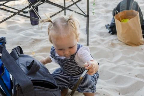 Curious toddler exploring a backpack on a sandy beach with beach gear 스톡 사진