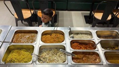 Curious toddler exploring buffet selection with noodles pasta and rice dishes 스톡 동영상 337990962