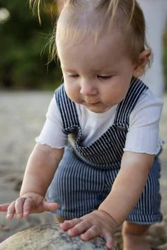 Curious toddler exploring a rock on a sandy beach during a sunny day 스톡 사진