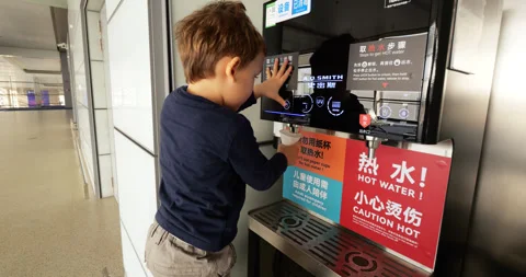 Curious toddler operating high-tech public water dispenser at Chinese airport Stockbeeldmateriaal 346521224
