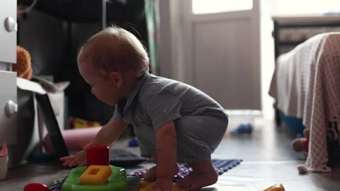 A curious toddler playing with colorful plastic stacking toys on the floor in a Stock Footage 345611595