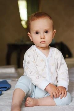 Curious toddler sitting on a bed in soft morning light Stock Photos