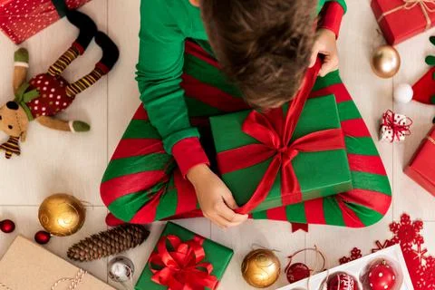 Curious young boy in pajamas sitting on the floor, opening christmas present. Stock Photos
