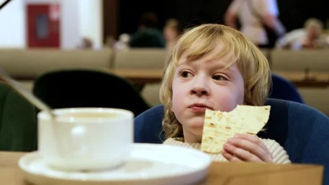 Curly blond boy eats flatbread in cafe Video stock 305141198