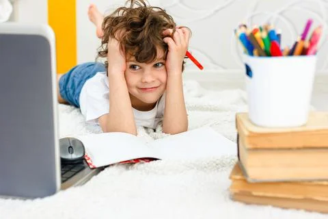 Curly boy is engaged at computer. schoolboy looks up, view into camera. Stock Photos