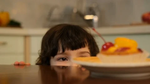 Curly boy peeking from the table and stealing cake with red cherry Stock Footage 125705987