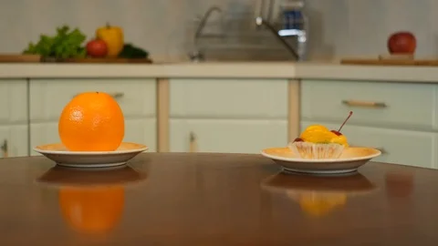 Curly boy peeking from the table and choosing between cake or an orange Stock Footage 125706693