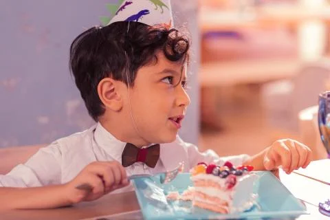 Curly boy talking while eating his piece of cake Foto stock
