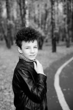 Curly brown-haired boy with a mohawk hairstyle in a leather jacket against th Stock Photos