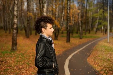 Curly brown-haired boy with a mohawk hairstyle in a leather jacket against th Stock Photos