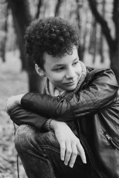 Curly brown-haired boy with a mohawk hairstyle in a leather jacket against th Stock Photos