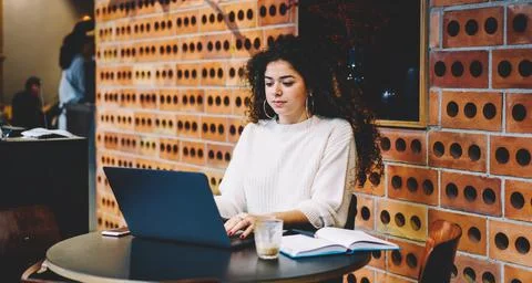 Curly female programmer checking software text during laptop working on distance Stock Photos