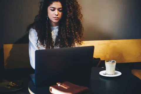 Curly female programmer checking software text during laptop working on distance Stock Photos