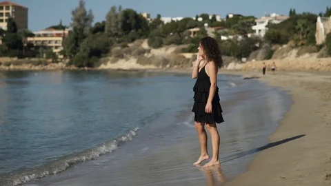 Curly girl talking on the phone on the coast near the ocean Stock Footage