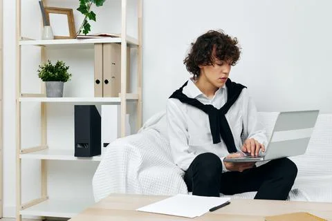 Curly guy sitting on the couch at the table in front of a laptop Lifestyle Stock Photos