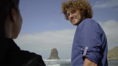 Curly guy smiles looking at his girlfriend while walking along the ocean 스톡 동영상 219349124