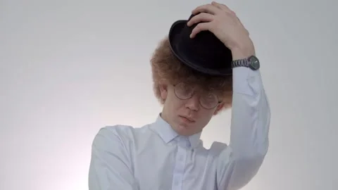 Curly guy takes off his hat while sitting on a chair Stock Footage 146576478