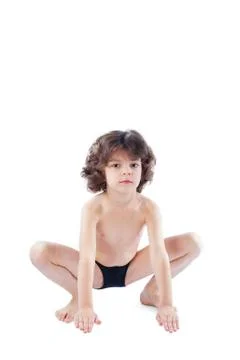 The curly-haired boy in a bathing suit sits in a pose of a frog looking at th Stock Photos