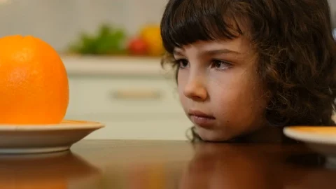 Curly-haired boy takes an orange from the table. Healthy food Stock Footage 125706348
