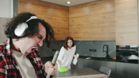 A curly-haired brunette man in checkered shirt with headphones sings and dances Video stock 296833670