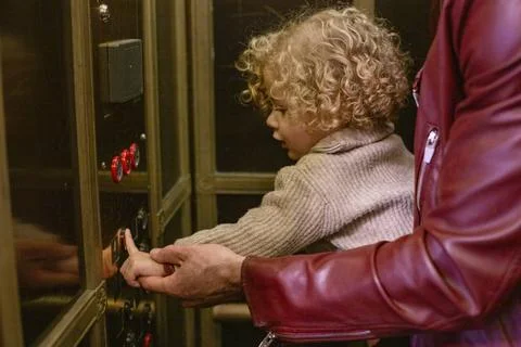 Curly-haired child learning to press an elevator button with the help of a... Foto stock