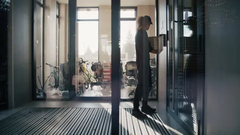 Curly-Haired Courier Delivering Parcel Inside Modern Building Entrance Stockbeeldmateriaal 322513543