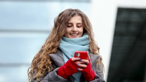 Curly-haired female using smartphone standing outside. A smiling happy girl Stock Footage 194431147