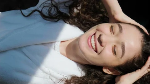 Curly haired girl looking at camera with charming smile, play with sun rais. Video stock 153108466