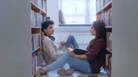 Curly-Haired Guy and Dreadlocked Girl Reading and Talking on the Floor 库存影片 335131334