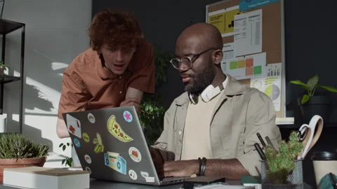 Curly-Haired Guy Asking Male Colleague who Working on Laptop about Project Stock Footage 299207812