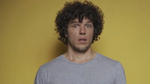 Curly-haired guy with a beard depicts surprise in the studio. Young man not Stock Footage 142213980